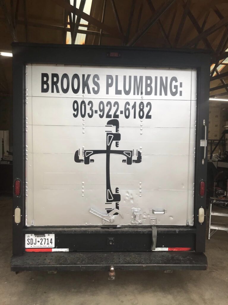 Back of Brooks Plumbing box truck with logo, phone number, and pipe-shaped cross graphic